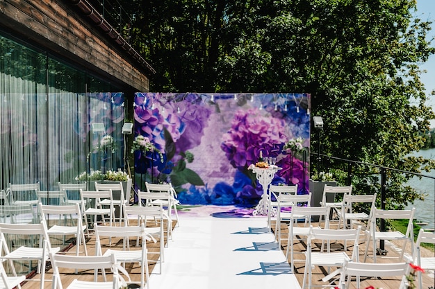 Hochzeit einrichten. Dekor. Holzstühle im Bankettbereich im Hinterhof. Bogen für Hochzeitszeremonie a ist mit Blumen und Grün, Grün geschmückt.