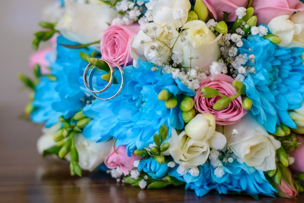 Hochzeit Goldringe und Hochzeitsstrauß von blauen, weißen und rosa Blumen auf einem Holztisch