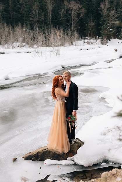 Hochzeit im winter, braut und bräutigam stehen am ufer eines gefrorenen flusses und umarmen sich.