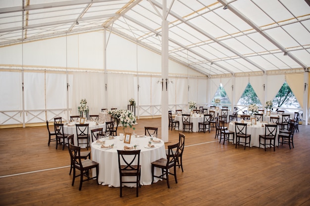 Hochzeit im Zelt. Dekoration der Halle. Weiße Tischdecken, schönes Dekor und Geschirr.