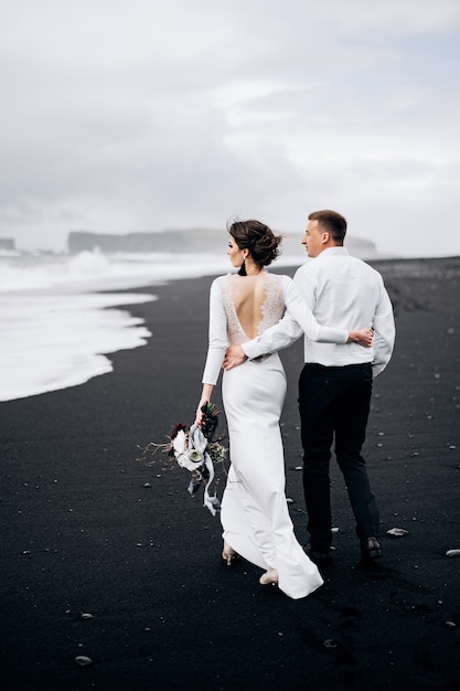 Hochzeit in Island Ein Hochzeitspaar geht am schwarzen Strand von Vic Sandstrand entlang