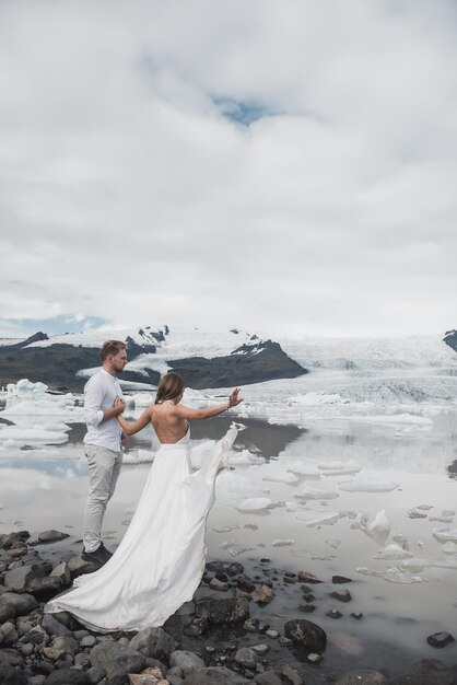 Hochzeit in Island. Ein Mann und ein Mädchen in einem weißen Kleid umarmen sich, während sie auf einem blauen Eis stehen