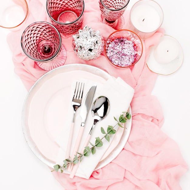 Hochzeit oder festliche Tischdekoration. Teller, Weingläser, Kerzen und Besteck mit dekorativem Textil auf weißem Hintergrund. Schönes Arrangement auf rosa Farbe