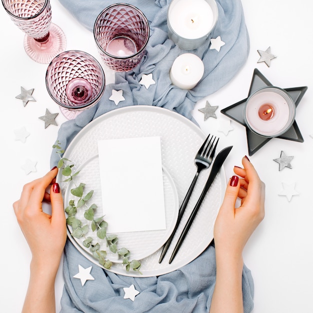 Hochzeit oder festliche Tischdekoration. Teller, Weingläser, Kerzen und Besteck mit grauem dekorativem Textil auf weißem Hintergrund. Schöne Anordnung.