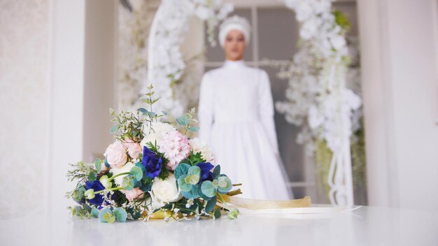 Hochzeitsblumen auf dem Tisch vor der jungen muslimischen Braut im weißen Kleid, die im Bogen steht