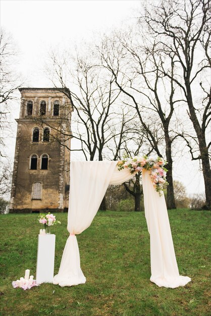 Hochzeitsbogen mit Stoff und Blumen im Freien verziert. Schöne Hochzeit eingerichtet. Hochzeitszeremonie auf grünem Rasen im Garten.