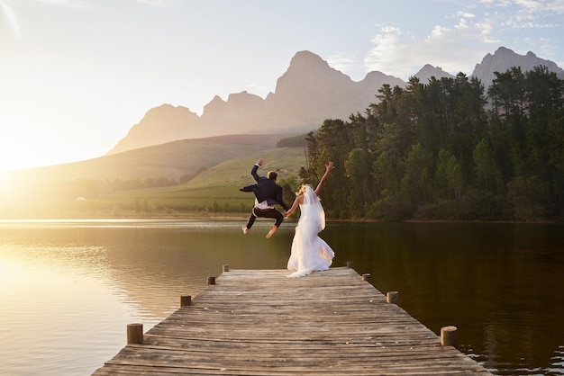 Hochzeitsbraut und Bräutigam springen zusammen mit Leidenschaft, Liebe und Romantik in den See. Verrückte, lustige Ehe und glückliches Paar auf dem Pier, um romantische Liebesbeziehungen in der Natur und im Wasser von hinten zu feiern