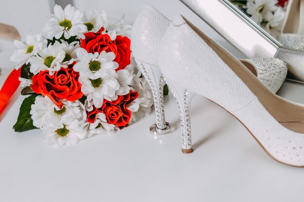 Hochzeitsdekor, Details des Morgens der Braut. Weiße Schuhe in Strasssteinen und Eheringen