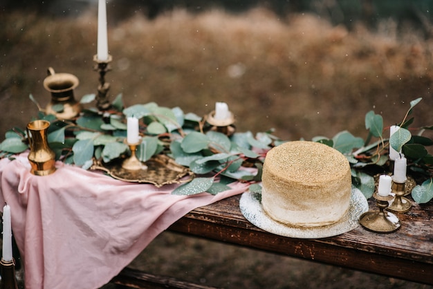 Hochzeitsdekoration mit einem goldenen kuchen auf einer holzbank vor einem wasserfallhintergrund