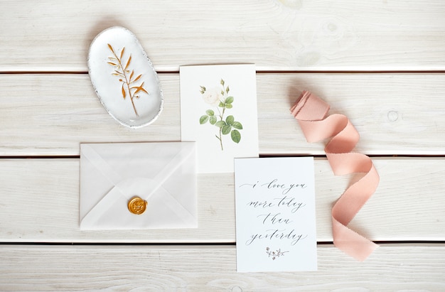 Hochzeitseinladung als verzierter Brief auf einer weißen Tischdecke mit einem Blumenarrangement.