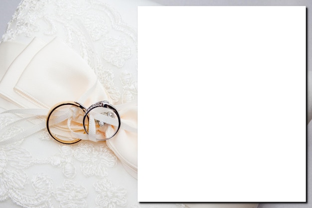 Hochzeitseinladungskartenschablone der leeren leeren Papierkarte der Draufsicht mit goldenen Ringen der Ehe an auf weißem Brautkleidhintergrund