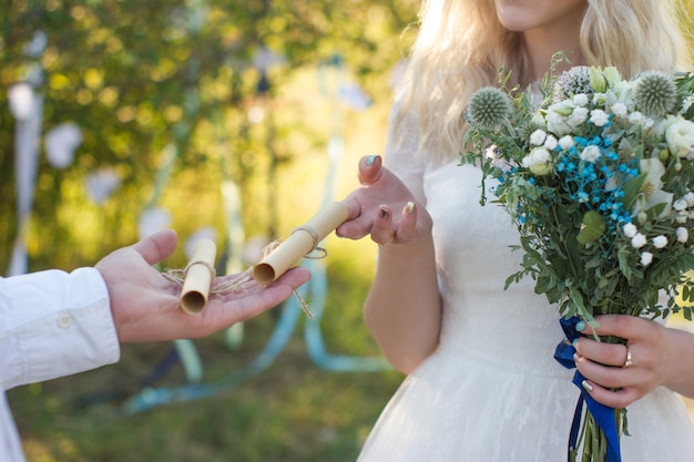 Foto hochzeitsgelübde auf gerolltem papierblatt auf dem rustikalen hochzeitskonzept des bräutigampalmenhochzeitsblumenstraußes im freien