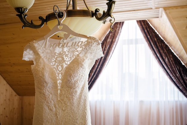Hochzeitskleid hängt an einem Kronleuchter in einem Hotelzimmer