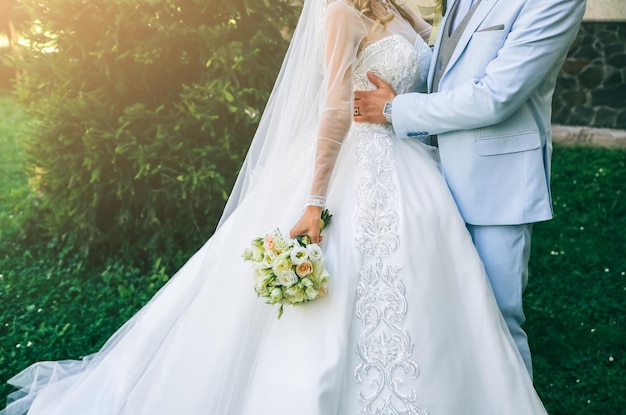 Hochzeitspaar in der Liebe geht im Freien Bräutigam im blauen Anzug und Braut im Luxuskleid Schöner Blumenstrauß in den Händen