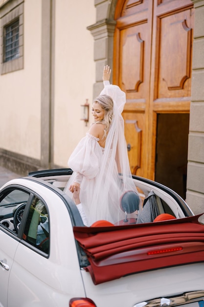 Hochzeitspaar in einem Cabrio, die Braut tanzt auf dem Sitz, der Bräutigam fährt eine Autohochzeit