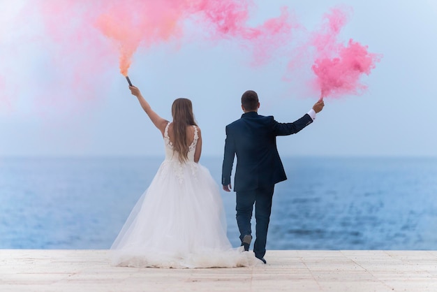 Hochzeitspaar mit farbigen Rauchfackeln und dem blauen Meer und dem Himmel im Hintergrund