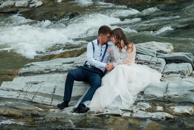 Hochzeitspaar umarmt sich in der Nähe des Gebirgsflusses. Braut und Bräutigam . Schöne Blumen. Hochzeitsfotoshooting in der Natur.