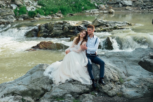 Hochzeitspaar umarmt sich in der Nähe des Gebirgsflusses. Braut und Bräutigam . Schöne Blumen. Hochzeitsfotoshooting in der Natur.