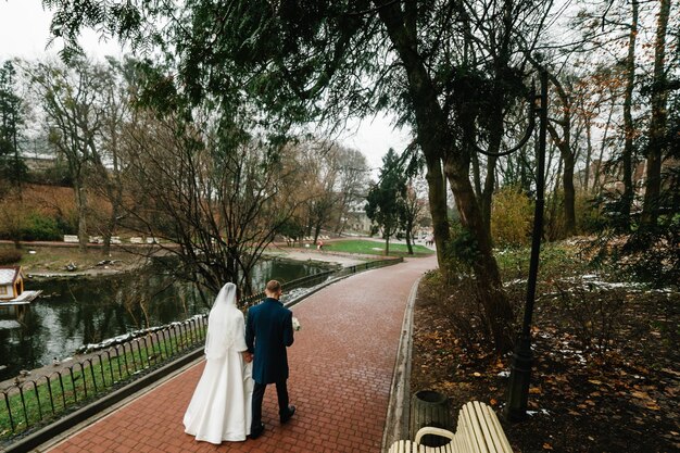 Hochzeitspaar zu Fuß zurück in die Natur Braut in einem Kleid und Bräutigam gehen in einem grünen Park Rückansicht