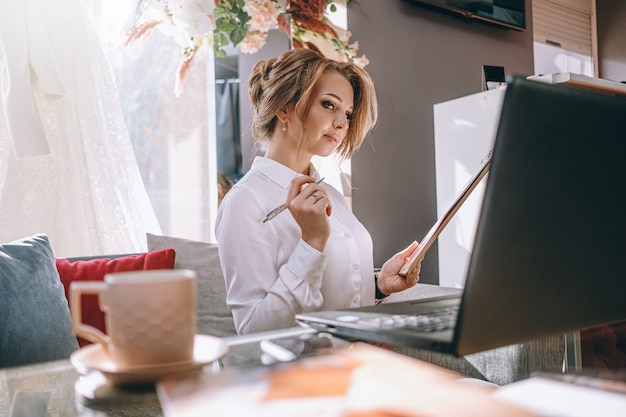 Hochzeitsplaner der jungen Frau im Büro mit Laptop und Tablette zum Schreiben