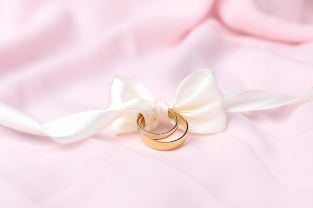Hochzeitsringe, die mit einem Band auf einem rosa Tuch in Nahaufnahme gebunden sind