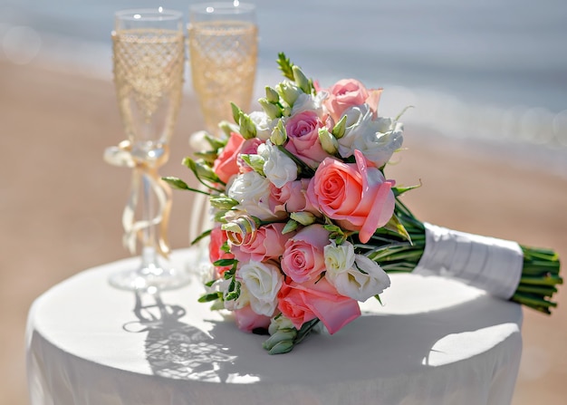 Hochzeitsstrauß auf dem Tisch neben den Gläsern. Blumen auf einem Hintergrund von Sand und Wasser.