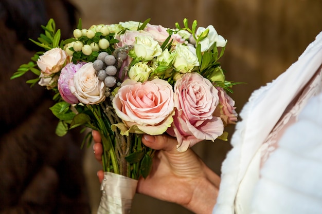 Hochzeitsstrauß aus Rosen mit einem rosa Band in den Händen der Braut, die Braut hält einen Hochzeitsstrauß aus Rosen