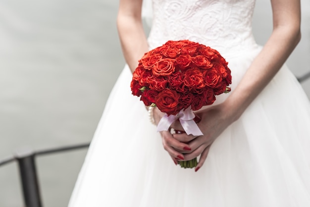 Hochzeitsstrauß aus roten Rosen in den Händen der Braut