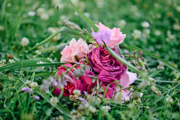 Hochzeitsstrauß mit lila und rosa Rosen, violette Blumen, die auf einem grünen Gras liegen