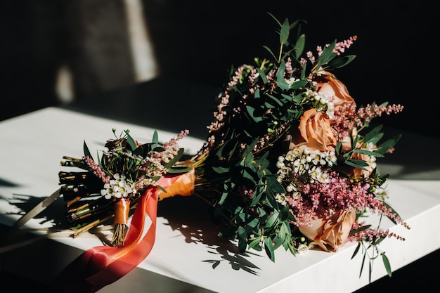 Hochzeitsstrauß mit Rosen auf dem Tisch und einer Boutonniere.Die Dekoration bei der Hochzeit