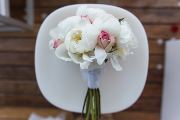 Hochzeitsstrauß mit Rosen und Pfingstrosen liegt auf einem weißen Stuhl