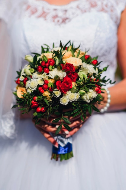 Hochzeitsstrauß mit roten Rosen und Gänseblümchen in den Händen der Braut