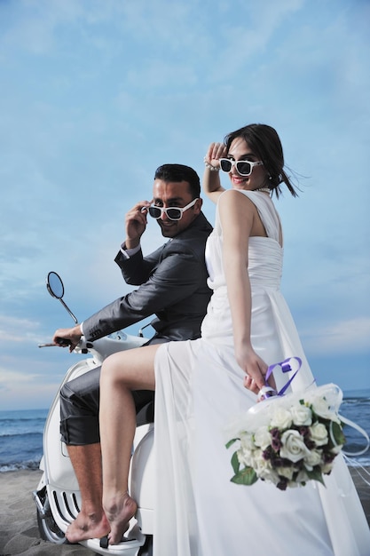 Hochzeitsszene von Braut und Bräutigam frisch verheiratetes Paar am Strand fahren weißen Roller und haben Spaß