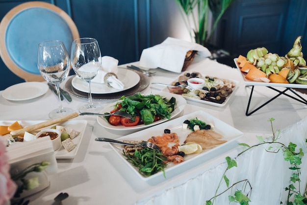 Hochzeitstisch mit Vorspeisen. Hochzeitstisch mit weißer Tischdecke, serviert mit gesundem Grün, kalter Fischplatte, Käseplatte und Obstplatte.