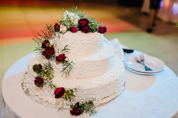 Hochzeitstorte Eine klassische gestufte weiße Torte, die mit Blumen auf dem Tisch geschmückt ist