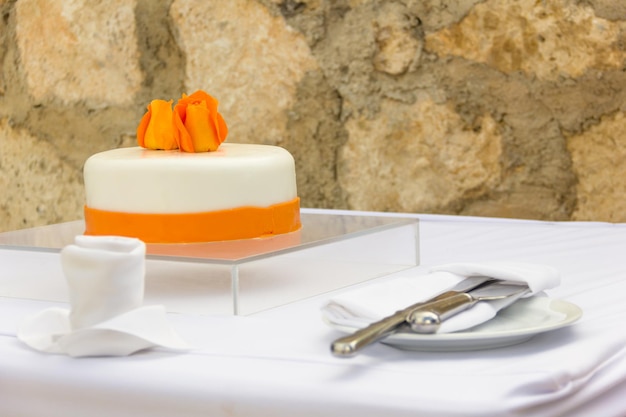 Hochzeitstorte mit orangefarbenen Blumen und Service auf weißer Tischdecke. Hochzeitsfeier für Braut und Bräutigam