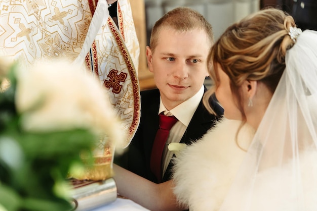 Hochzeitszeremonie der glücklichen, eleganten blonden Braut und des stilvollen Bräutigams, die Hände an der Bibel halten und Gelübde in der alten Kirche ablegen