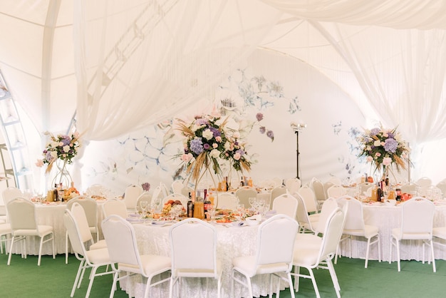 Hochzeitszeremonie in einem wunderschönen Zeltsaal mit mit Blumensträußen geschmückten Esstischen