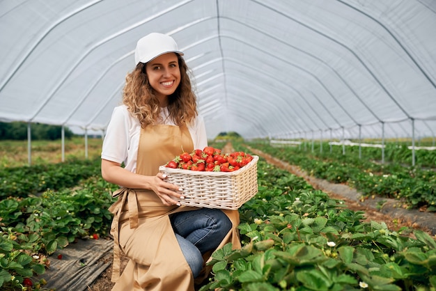 Hockende Frau hält Korb mit frischen Erdbeeren