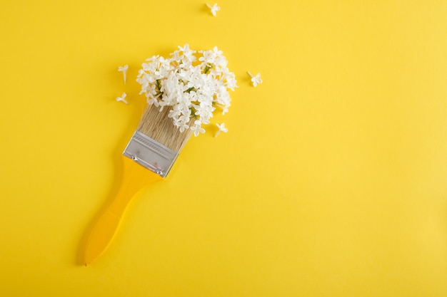 Hölzerne gelbe Pinsel und weiße Blumen von Flieder auf einem gelben Hintergrund Naturkunstkonzept Kopienraum