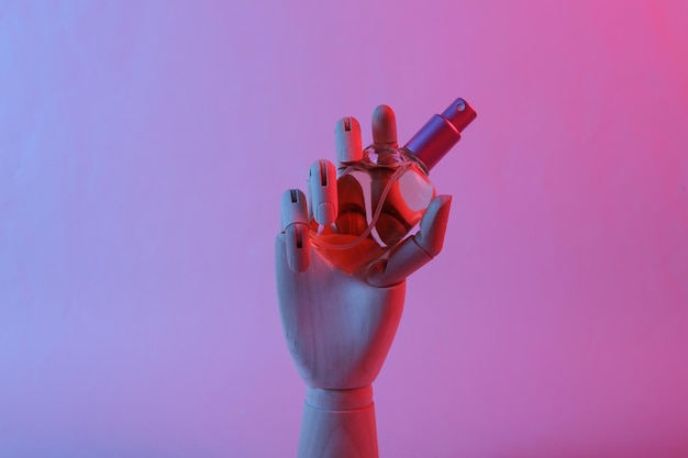 Hölzerne Hand, die Parfümflasche im Neonlicht des rosa blauen Farbverlaufs hält