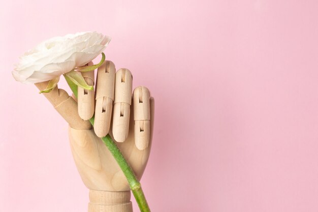 Hölzerne Hand mit einer weißen Blume auf einem Rosa