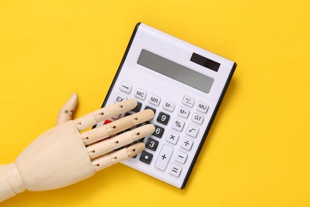 Hölzerne Hand mit Taschenrechner auf gelbem Hintergrund