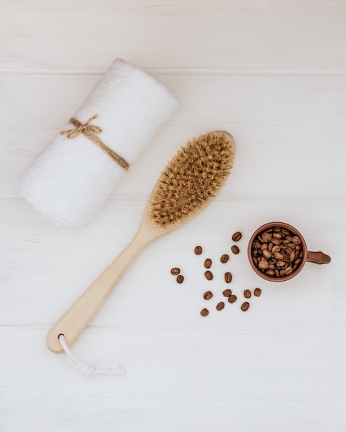 Hölzerne Körperbürste, weißes Handtuch und Kaffeebohnen auf einem weißen hölzernen Hintergrund.