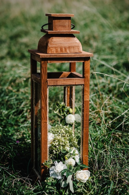 Hölzerne Laterne mit Blumen und viel Grün Vintage stilisierter schöner Kerzenhalter auf Natur Sommerhochzeitsdekor Straßenweise Hochzeitsdekoration im rustikalen Stil