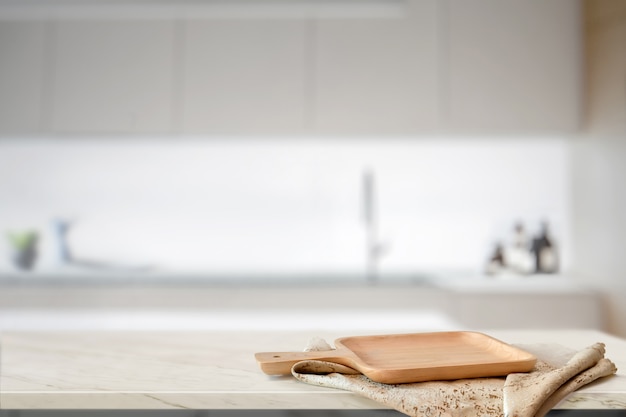 Hölzerne Platte auf weißer Tabelle im Küchenraumhintergrund und Kopienraum für Produkt- oder Lebensmittelmontage