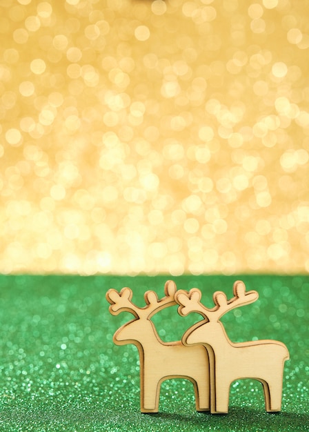 Hölzerne Rentierweihnachtsdekorationen auf glänzendem grünem und goldenem Hintergrund im Hochformat