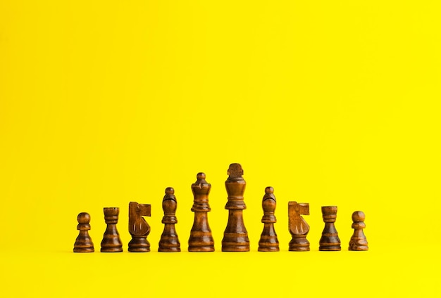 Hölzerne Schachfiguren, die in einer Reihe auf gelbem Hintergrund organisiert sind