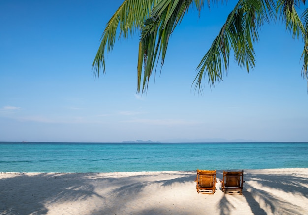 Hölzerne Sonnenliegen mit Palmblättern am Strand