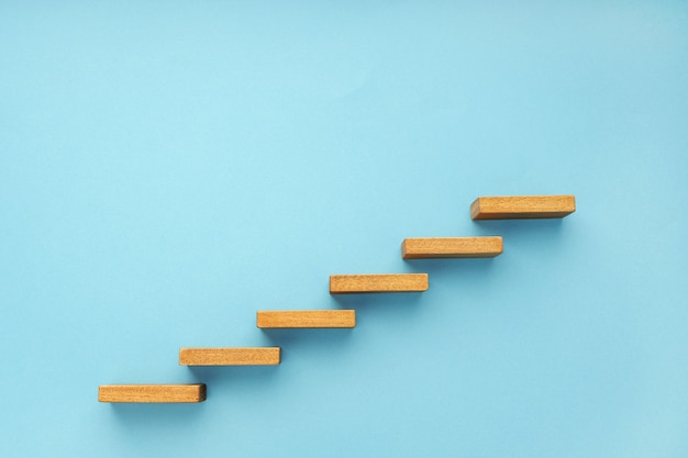 Hölzerne Treppe auf blauem Hintergrundwachstum, das Geschäftskonzeptkopienraum erhöht